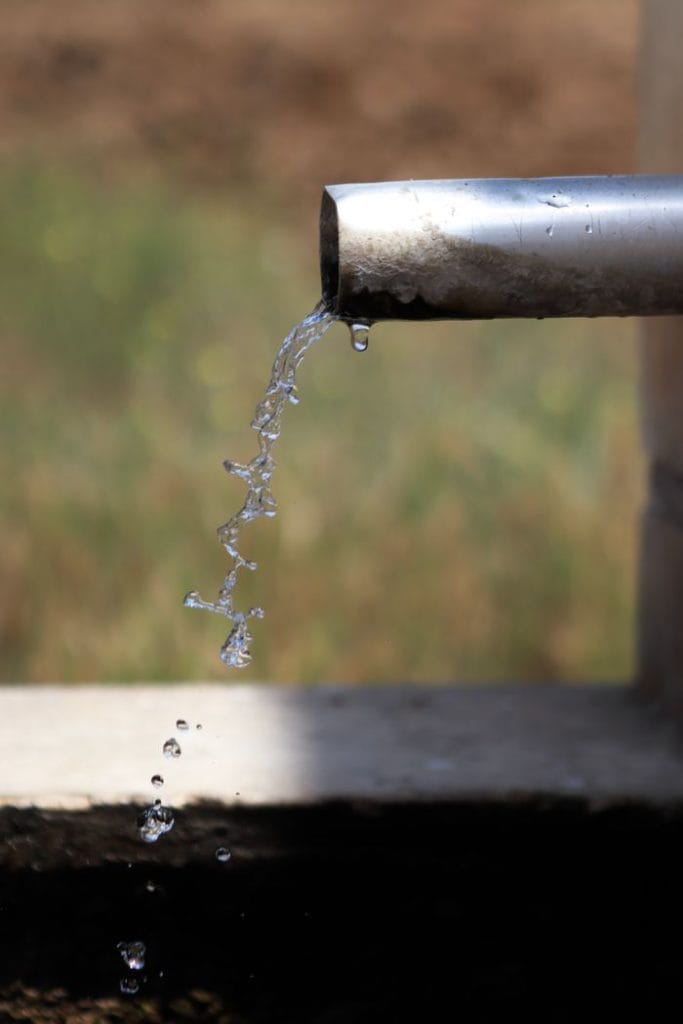 Clear water droplets flowing from an outdoor metal pipe in natural sunlight.